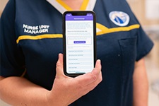 A person in a Rockingham Peel Group nursing uniform holds a mobile phone which displays the MyColonscopy app on the screen